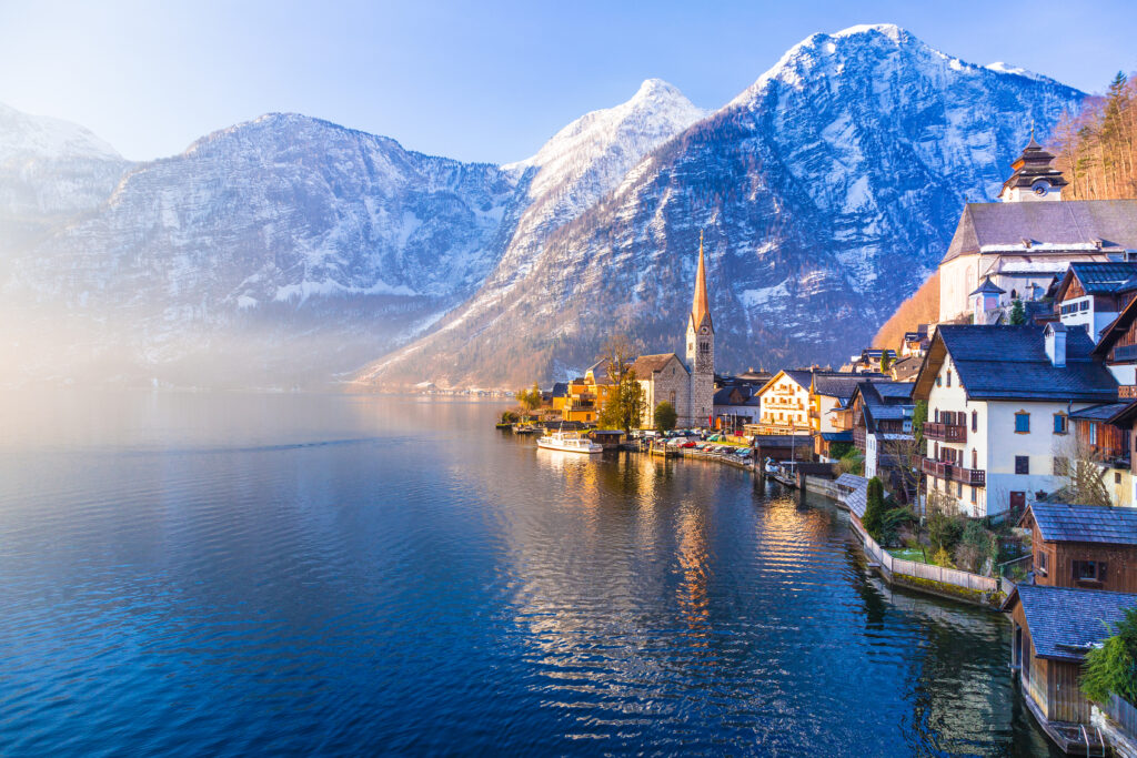 View of famous Hallstatt town with lake, mountains, and clear blue sky seen in one beautiful spring morning with golden morning light bathing the town
